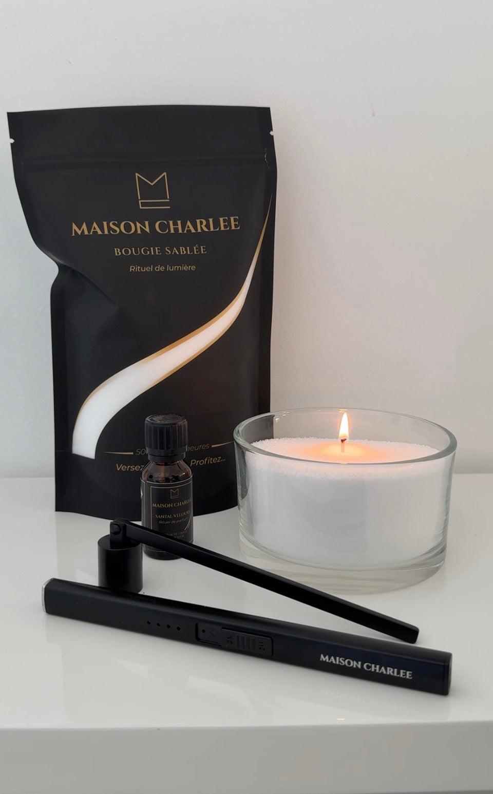 Bougie Blanc pur Maison Charlee allumée avec sable de bougie végétal, parfum de Grasse, briquet USB rechargeable et éteignoir.