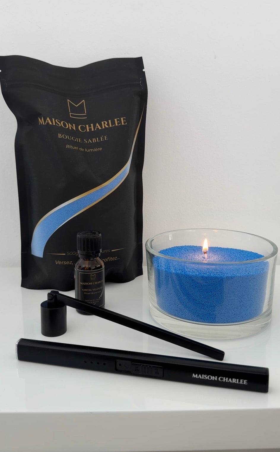 Bougie Bleu azur Maison Charlee allumée avec sable de cire végétale, parfum de Grasse, briquet USB rechargeable et éteignoir.
