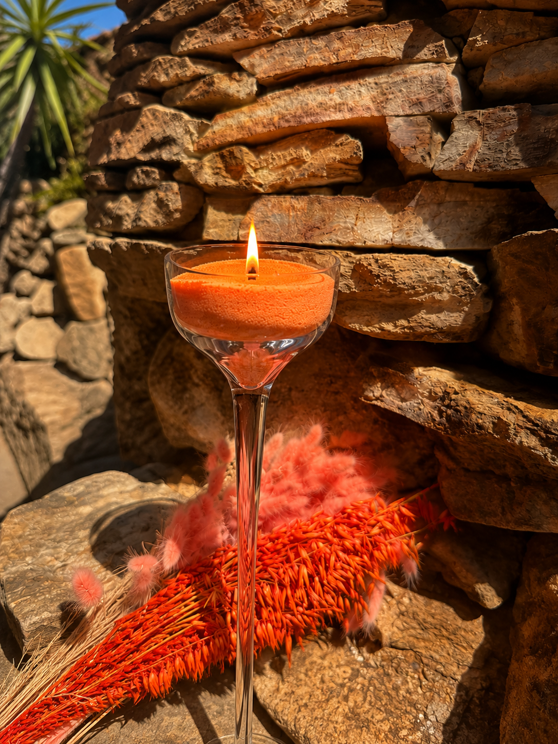 Bougie sablée orange allumée Maison Charlee dans un verre transparent sur fond de pierre naturelle