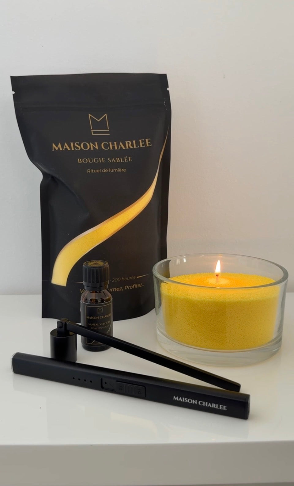 Bougie Jaune lumière Maison Charlee allumée avec sable de bougie végétal, parfum de Grasse, briquet USB rechargeable et éteignoir.
