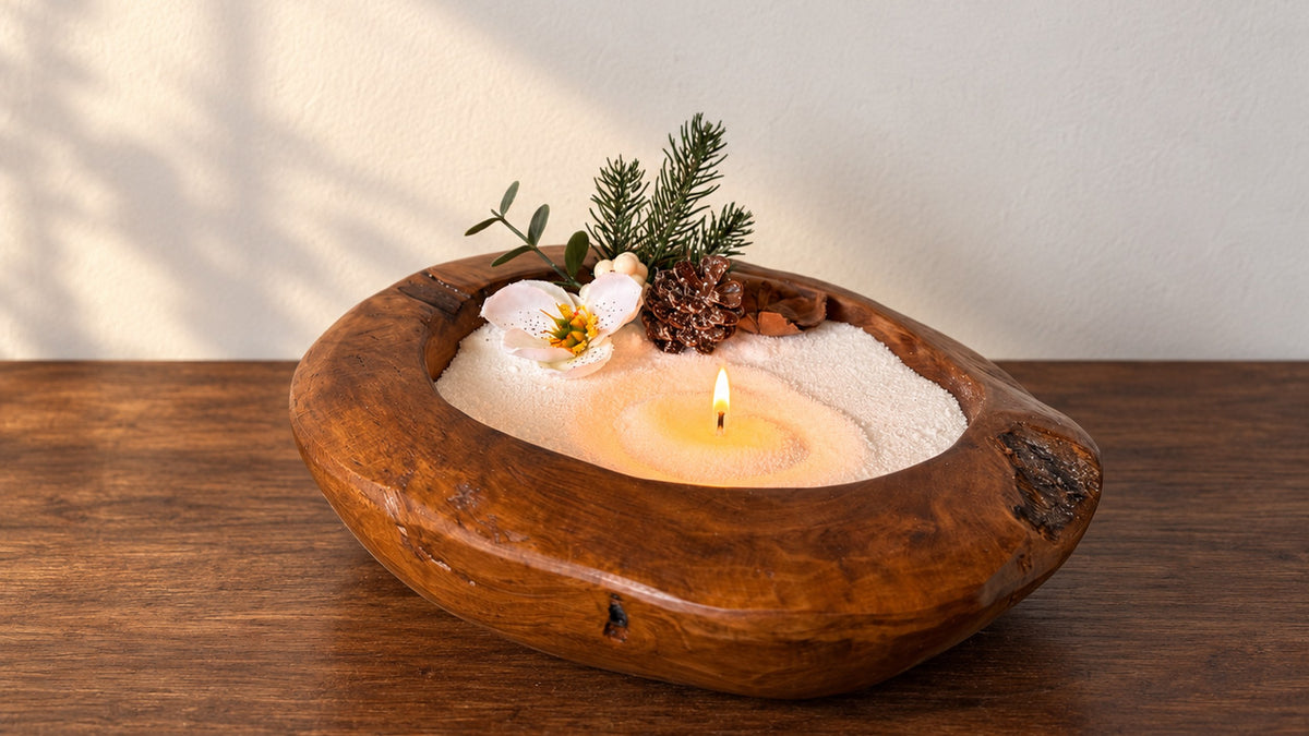 Bougie sablée blanche Maison Charlee allumée dans un bol en bois, décor de sapin et pomme de pin